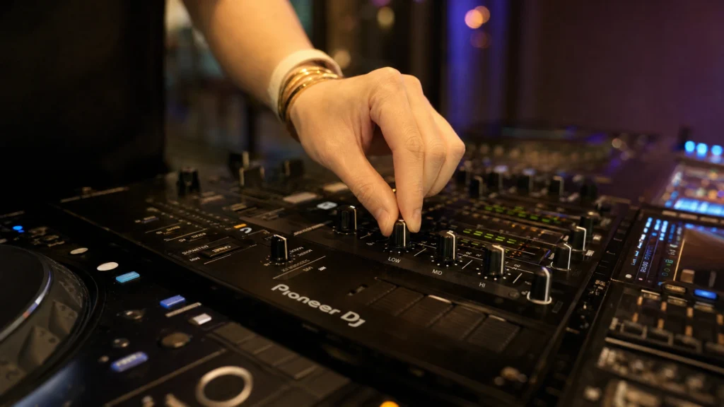 DJ adjusting low mid high EQ knobs on a mixer while mixing