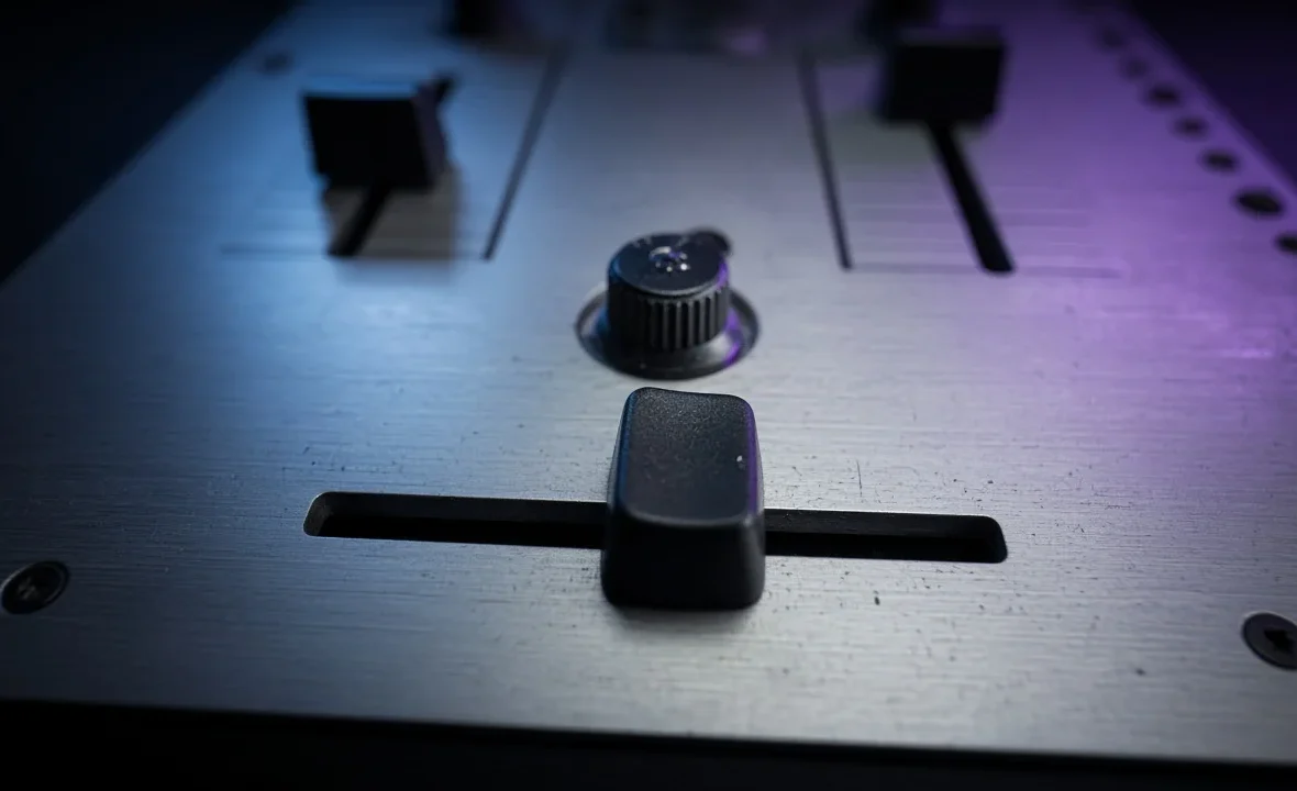 Close-up of a DJ mixer crossfader and curve knob in a dark DJ booth