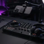 DJ controller with a phone on a tripod, laptop and audio interface set up for live streaming in a dark studio