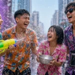 Young Thai friends in floral shirts laughing in a water fight on a Bangkok street during Songkran