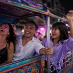 Young Thai friends laughing in the back of a tuk tuk on a glowing Bangkok street at night