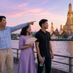 Young Thai adults in respectful dress on a riverside promenade with a porcelain temple spire glowing at golden hour